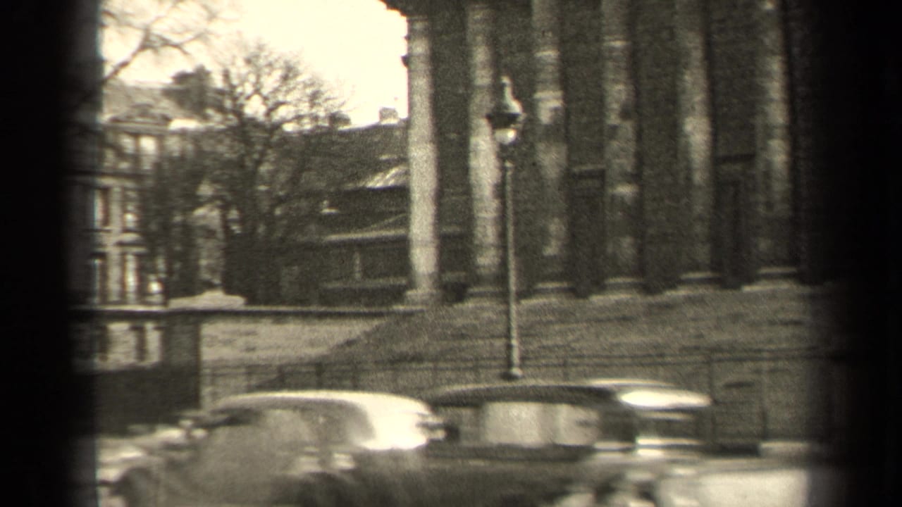 1947 Paris home-movie frame showing a columned building, street traffic and a partial riverside view in soft 8mm focus.