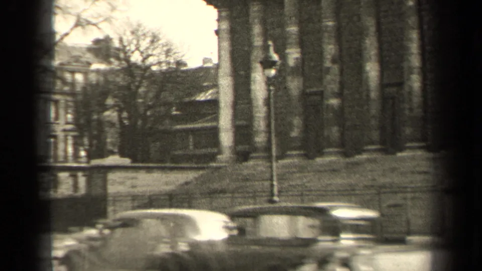 1947 Paris home-movie frame showing a columned building, street traffic and a partial riverside view in soft 8mm focus.