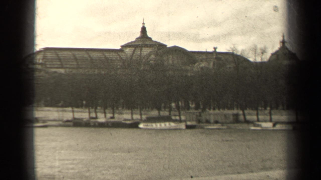 Riverfront view with leafless trees, moored boats and a large roofed building beyond.