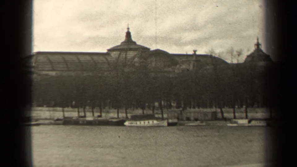 1947 Paris home-movie view of a formal riverfront building partly screened by trees, with boats along the embankment.