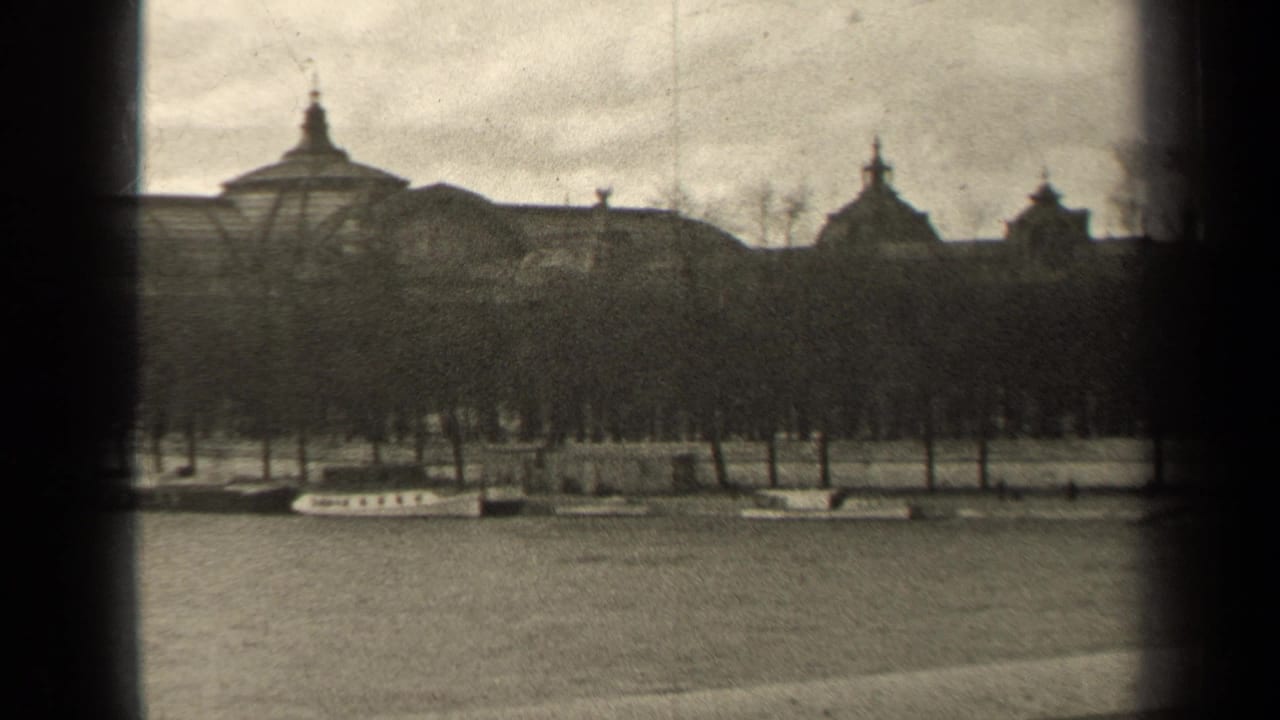 1947 Paris home-movie frame showing a winter park, leafless trees, pale paths, and distant domed rooftops in soft black-and-white 8mm.