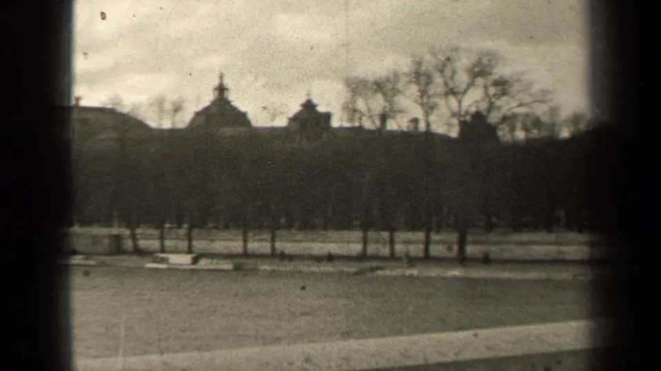 1947 Paris park landscape with winter trees, low paths, and distant historic roof forms seen through soft, grainy 8mm framing.