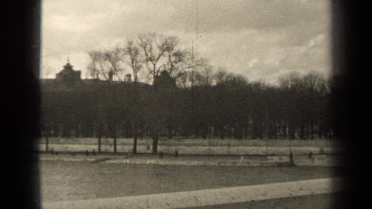 Black-and-white 8mm frame from Paris in 1947 showing winter trees, a park path, and muted rooftop silhouettes beyond the grounds.