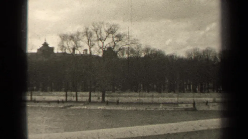 Black-and-white 8mm frame from Paris in 1947 showing winter trees, a park path, and muted rooftop silhouettes beyond the grounds.