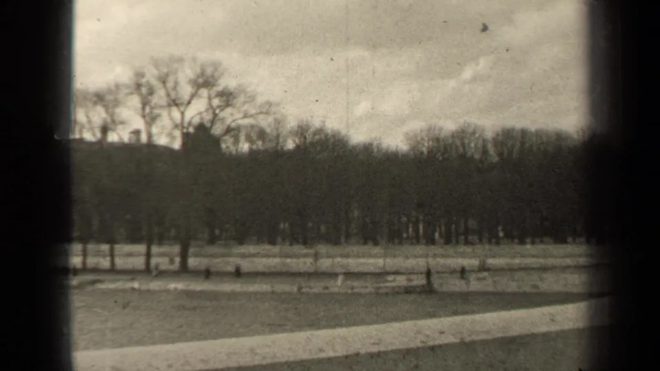 1947 Paris 8mm frame with a quiet winter park foreground, leafless trees, faint distant buildings, and visible film texture.