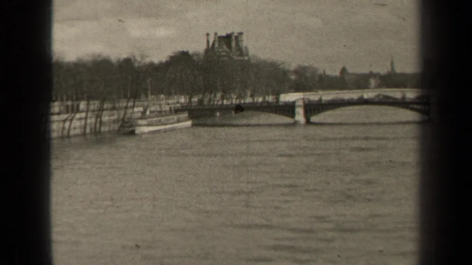 1947 Paris view along the Seine with an arched bridge, a riverboat near the bank, bare trees, and distant monuments.