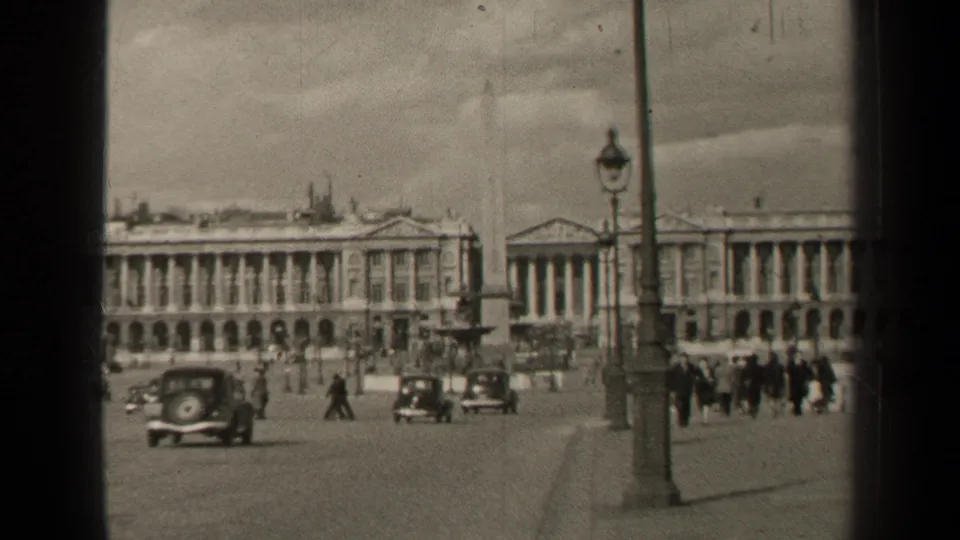 Paris, France in 1947, with mid-century cars, distant pedestrians, a streetlamp, obelisk base, and grand facades.