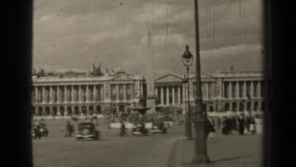 Mid-century Paris plaza footage showing moving cars, distant walkers, lampposts, and long neoclassical building fronts.