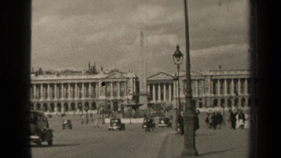 1947 Paris public square viewed through a window frame, with pedestrians and classic cars moving near an obelisk and neoclassical buildings.