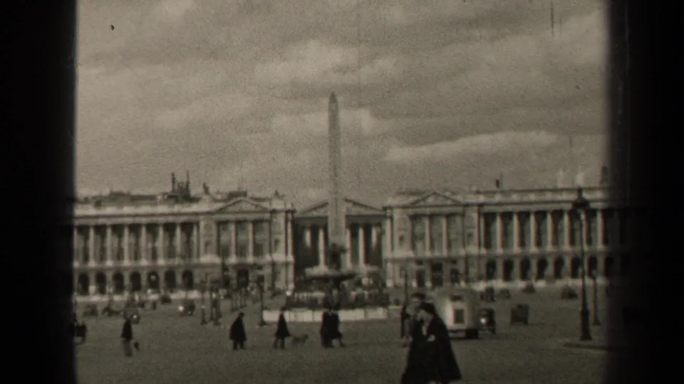 1947 Paris street-square view with pedestrians in dark coats crossing near cars, an obelisk, and large colonnaded buildings.