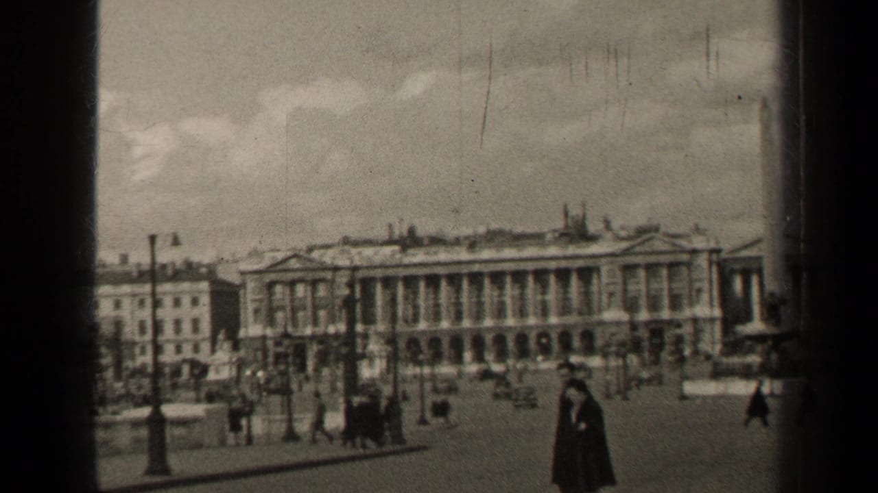 1947 Paris home-movie frame showing pedestrians in a broad square before large neoclassical buildings and street lamps.