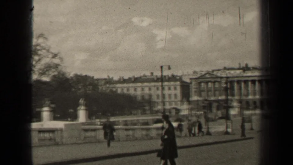 1947 Paris home-movie view of stone balustrades and pedestrians with trees and a columned building beyond.