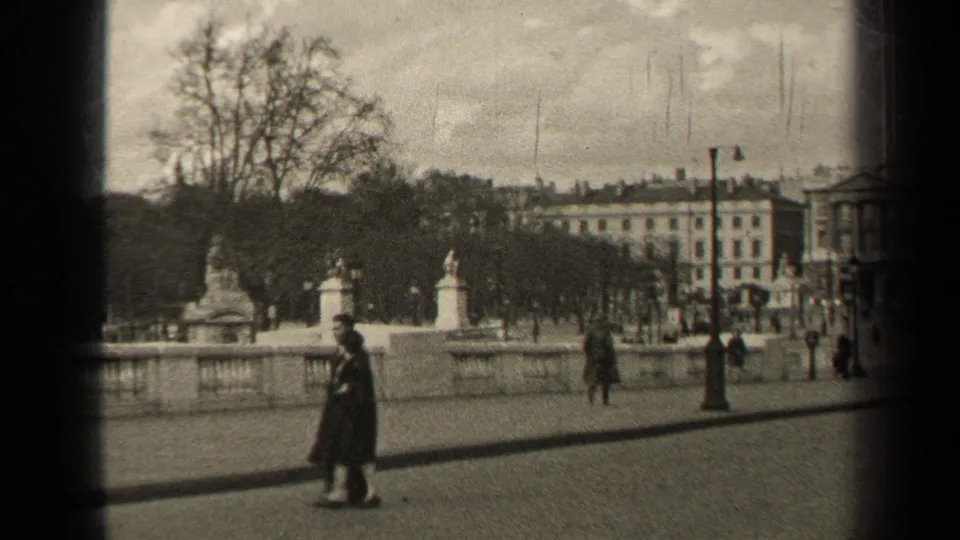 1947 Paris street view with pedestrians in coats, a wide paved walkway, bare trees, lampposts, and classical buildings in the distance.