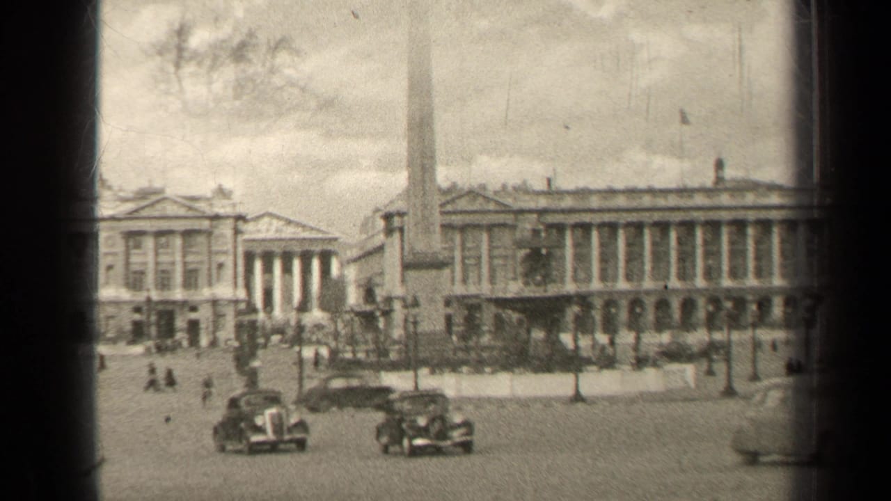 Vintage cars pass through a city square with an obelisk and columned buildings.