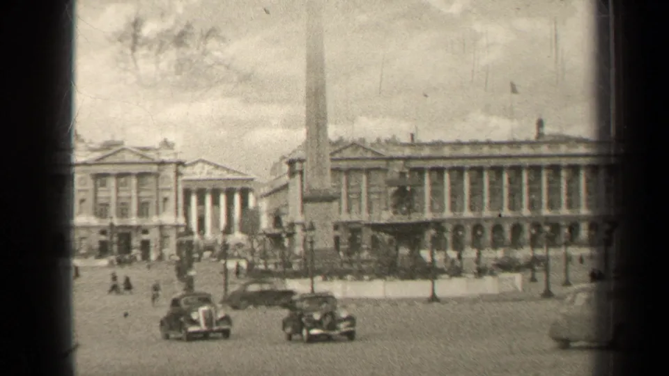 1947 Paris square with vintage automobiles, an obelisk, lampposts, pedestrians, and large classical buildings behind it.