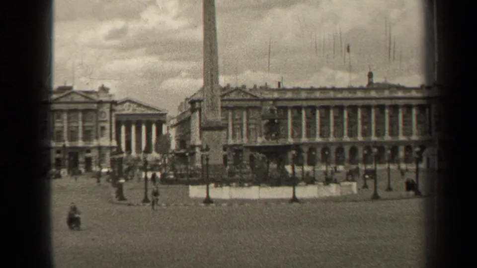 Black-and-white 8mm frame of a Paris public square in 1947, showing the obelisk, formal architecture, and distant people crossing the paving.