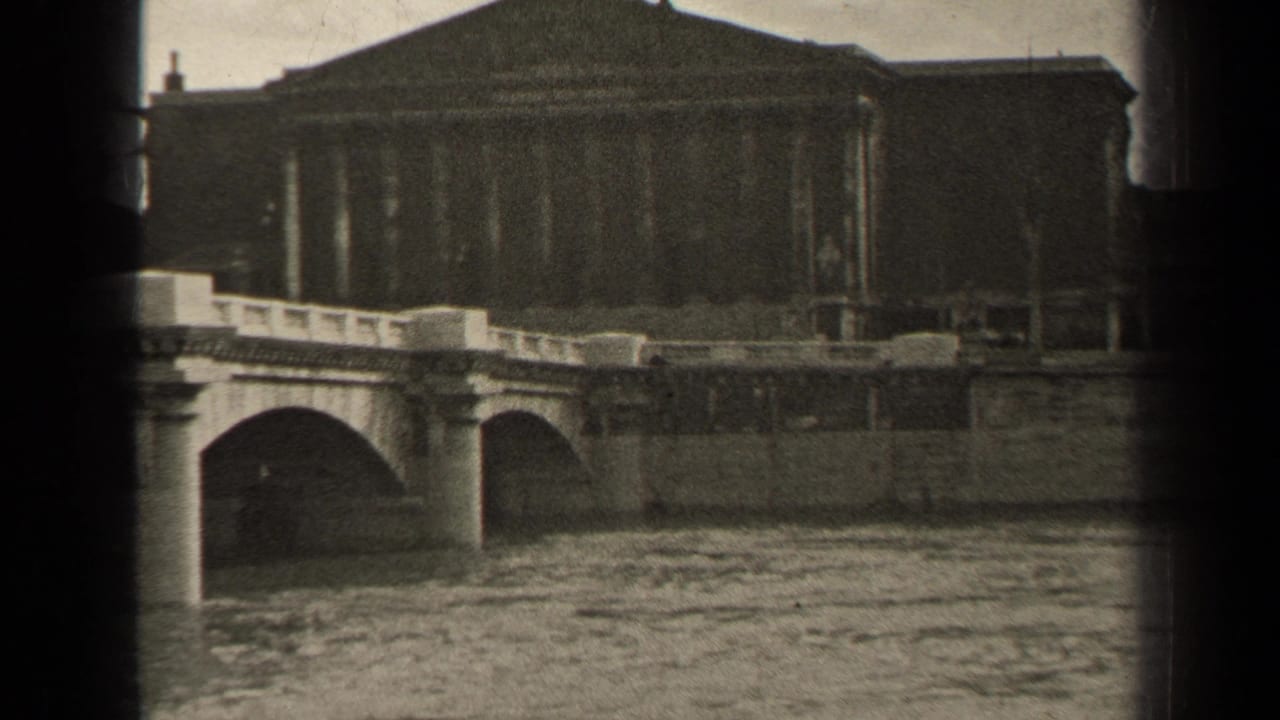 Stone bridge over a river with a large classical building in the background.