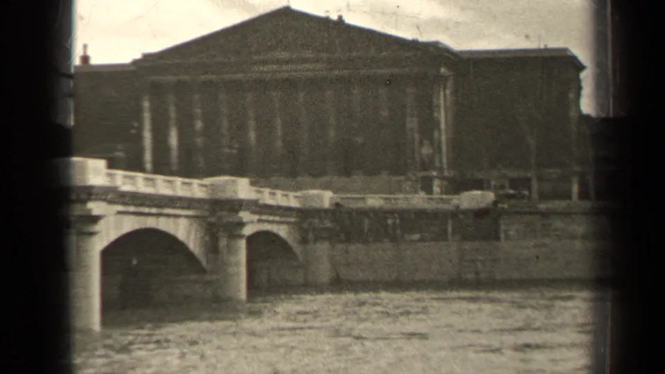 1947 Paris home-movie frame with the bridge, river wall, and large classical building filling most of the view.