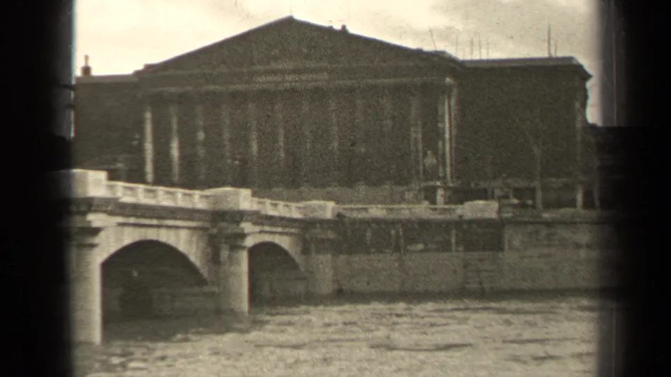 1947 Paris river scene with a stone bridge, embankment, and large neoclassical building seen in grainy 8mm footage.