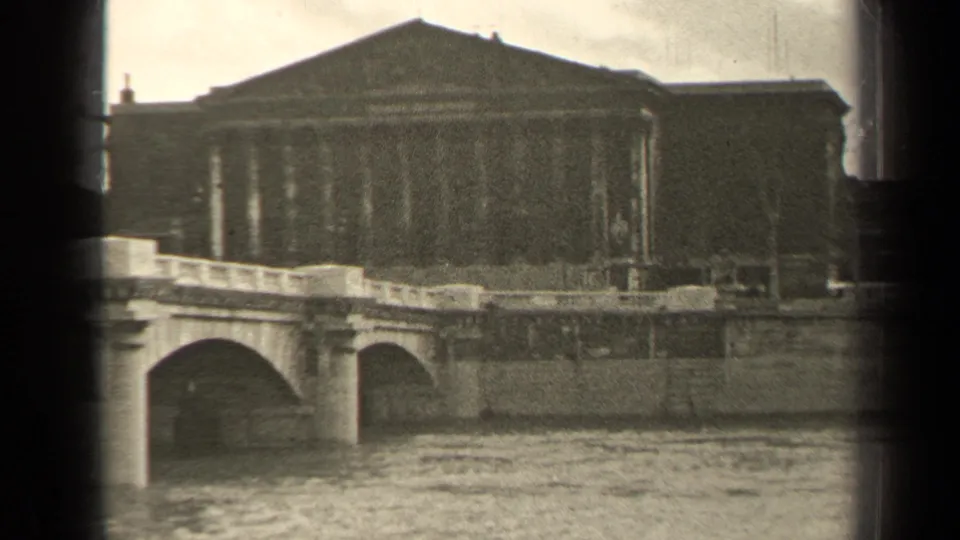 1947 Paris frame with a stone arch bridge crossing the river below a large classical facade.