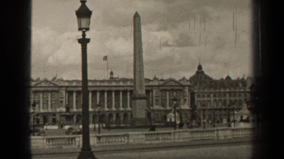 The Paris square remains in view, with the obelisk, foreground streetlamp, ornate facades, distant pedestrians, and light traffic.