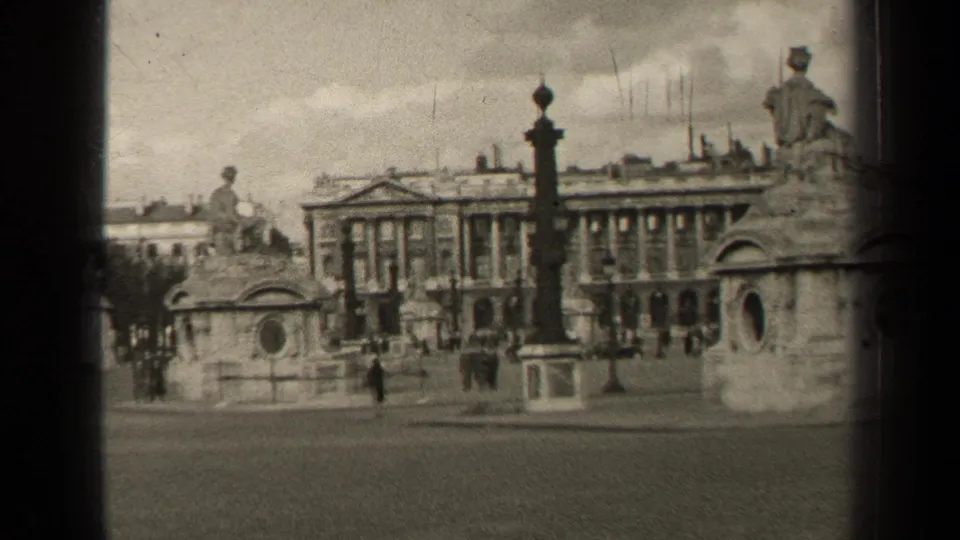 1947 Paris 8mm frame showing a broad street, distant pedestrians, stone monuments, statues, and a grand historic building facade.
