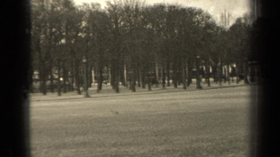 1947 Paris home-movie frame showing an open park lawn and bare tree line, partially obscured by dark window or gate edges.
