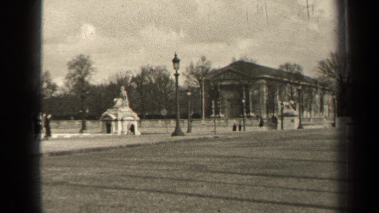 Small monument, lampposts, and a columned building across a park lawn.