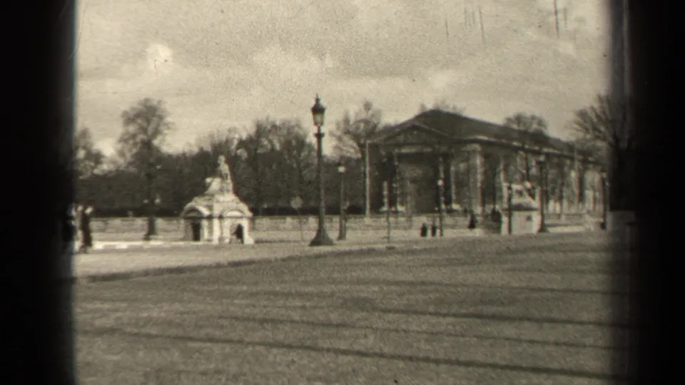 1947 Paris park view with a small monument, lampposts, bare trees, and a classical columned building in the background.