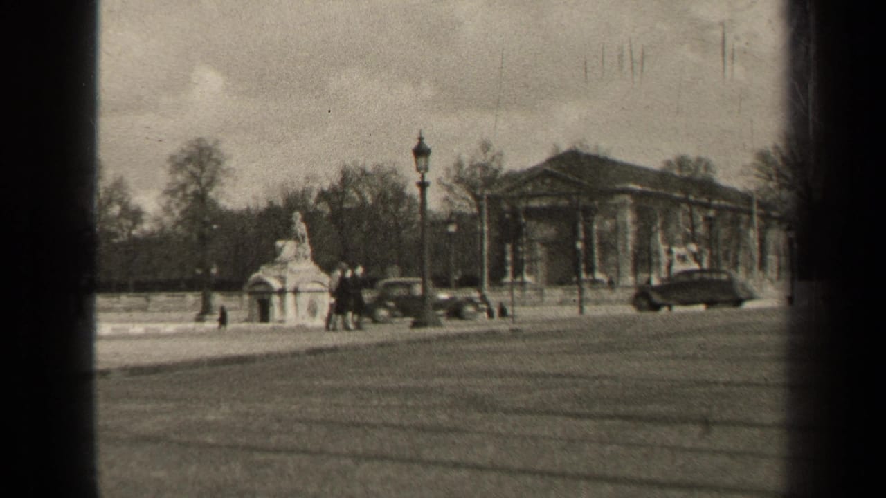 Wide Paris street with a stone monument, lamppost, pedestrians, and vintage cars near a columned building.