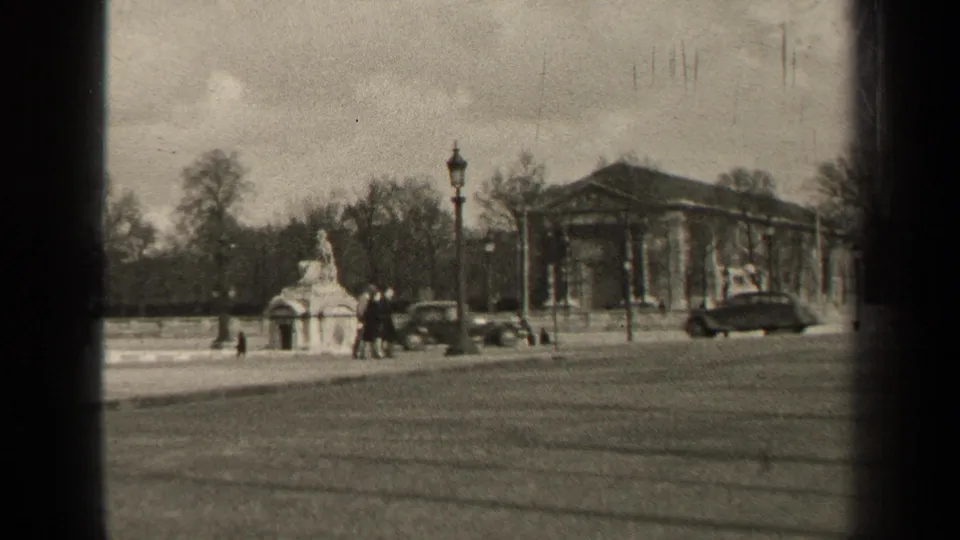 1947 Paris street view with a broad roadway, stone monument, pedestrians, vintage cars, bare trees, and a columned public building.