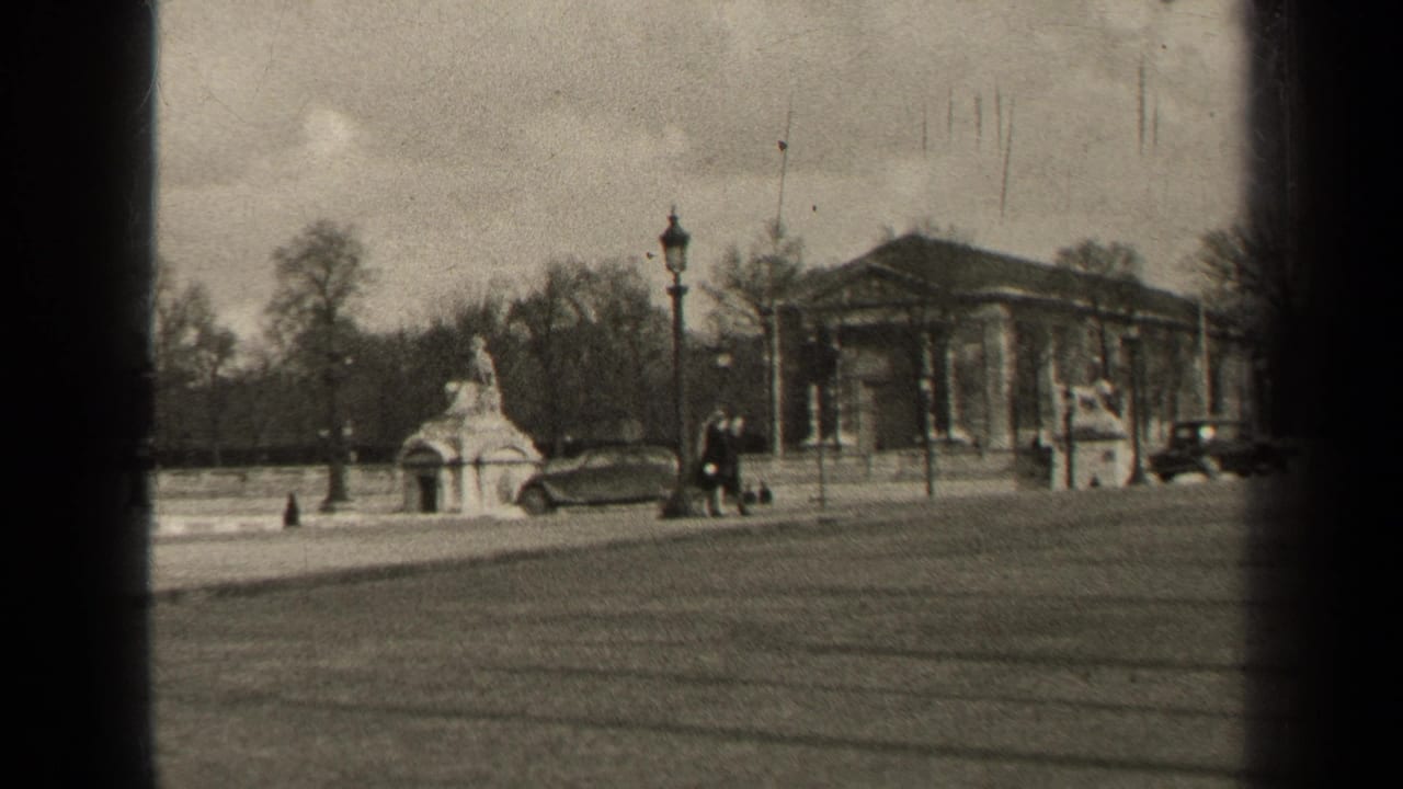 Broad street beside a monument and columned building, with pedestrians and cars passing through the frame.