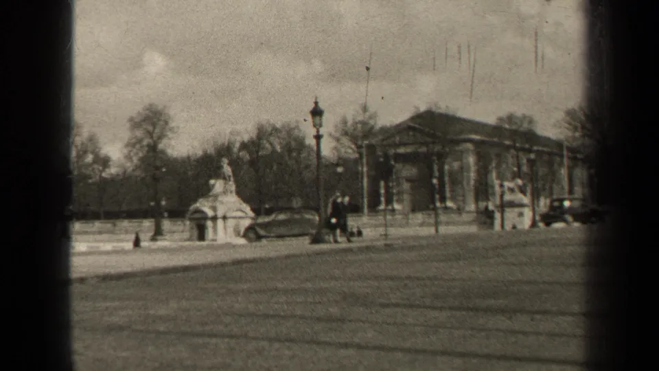 Paris, 1947, seen from across a broad street as pedestrians and mid-century cars pass a monument and columned building.