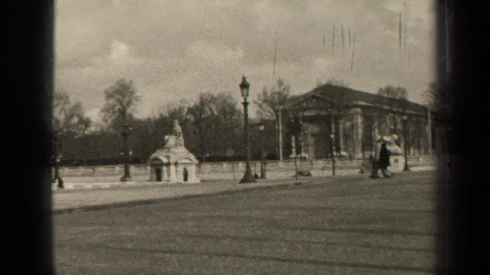 1947 Paris boulevard frame with a stone monument, tall lamppost, pedestrians on the pavement, bare trees, and a classical columned building.
