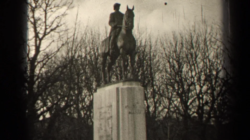 Soft black-and-white 8mm frame of a Paris equestrian monument, centered against bare trees and pale sky.