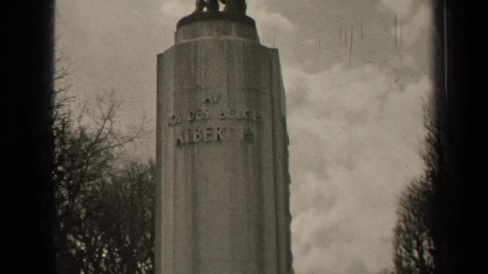 1947 black-and-white home-movie frame of a Paris monument pedestal with partial inscription and visible film scratches.