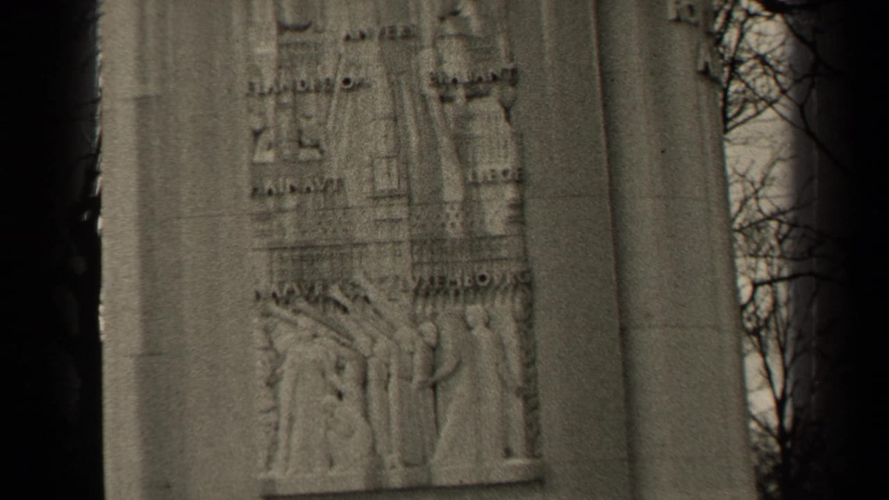1947 Paris 8mm frame showing a stone memorial panel with relief carving, inscriptions, and bare tree branches at the edge.