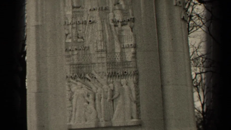 1947 Paris 8mm frame showing a stone memorial panel with relief carving, inscriptions, and bare tree branches at the edge.
