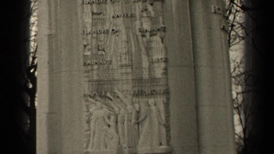 1947 Paris 8mm frame showing a closer handheld view of the memorial's carved stone figures and inscriptions beside bare branches.