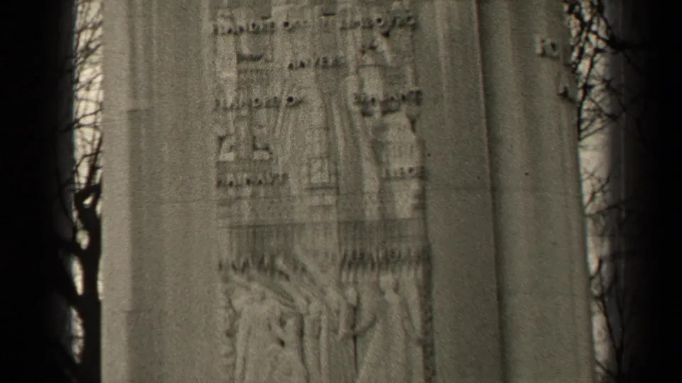 1947 Paris 8mm frame showing a soft close-up of a stone memorial relief with human figures, partial inscriptions, and tree branches.