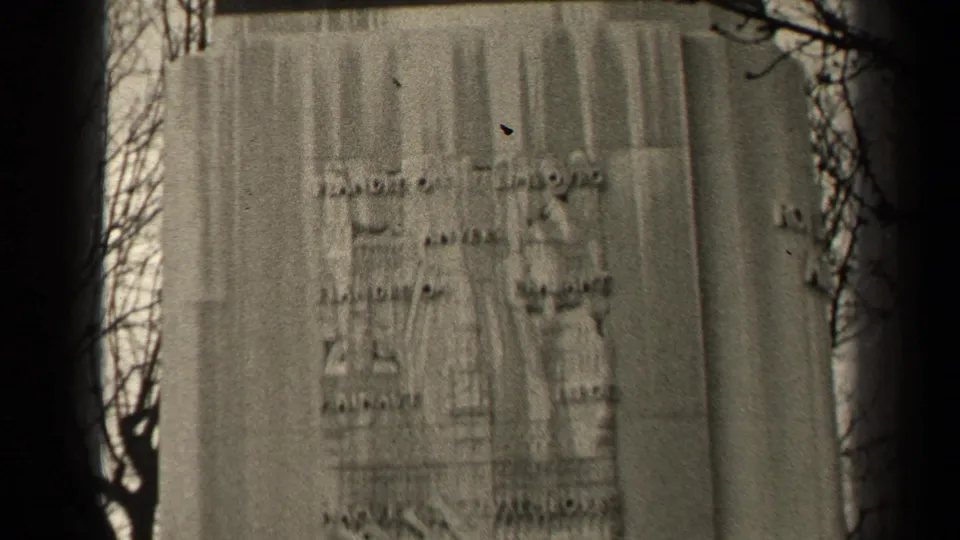 1947 Paris 8mm frame showing a weathered inscribed pedestal of an equestrian monument, with bare branches and soft focus.