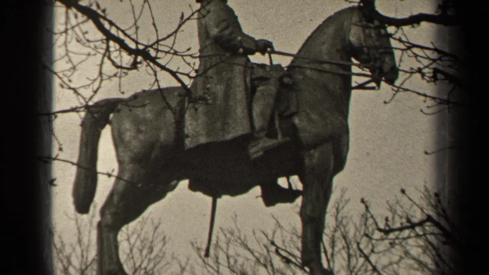 1947 Paris home-movie frame of an equestrian monument, with the horse and rider silhouetted by branches and pale sky.
