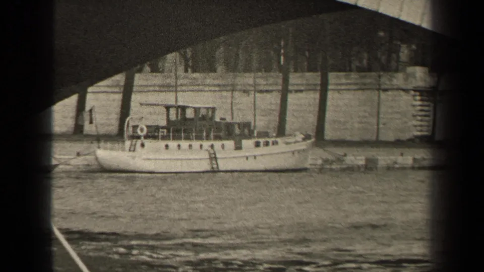 Final 1947 Paris frame of the small white boat on the river, seen below a bridge with a stone embankment and trees beyond.