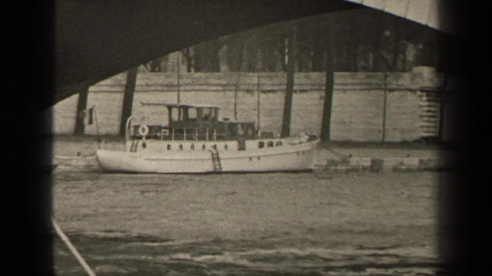 1947 Paris home-movie frame showing a small white motorboat moored along a riverbank under a bridge arch.