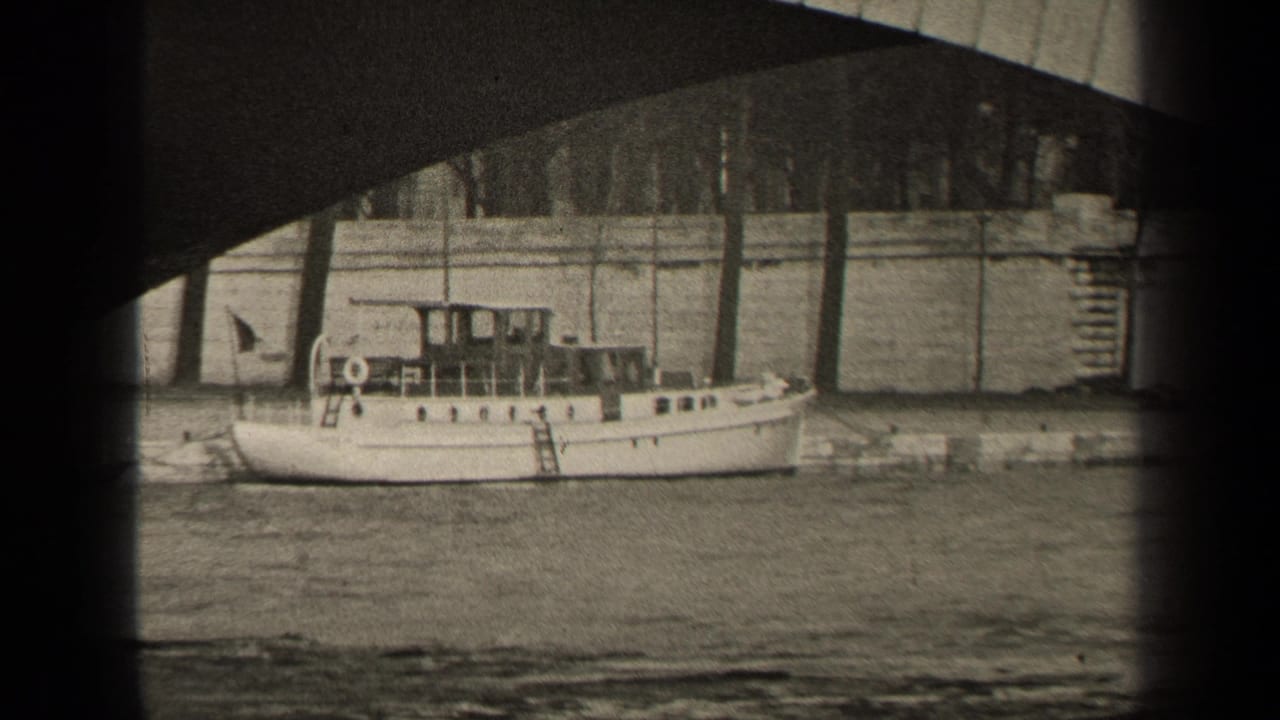 1947 Paris home-movie frame showing a white riverboat near a stone quay under a bridge, with riverside buildings in the background.