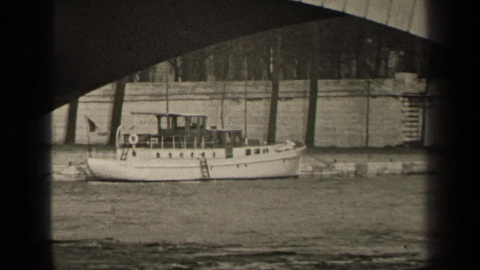 1947 Paris home-movie frame showing a white riverboat near a stone quay under a bridge, with riverside buildings in the background.
