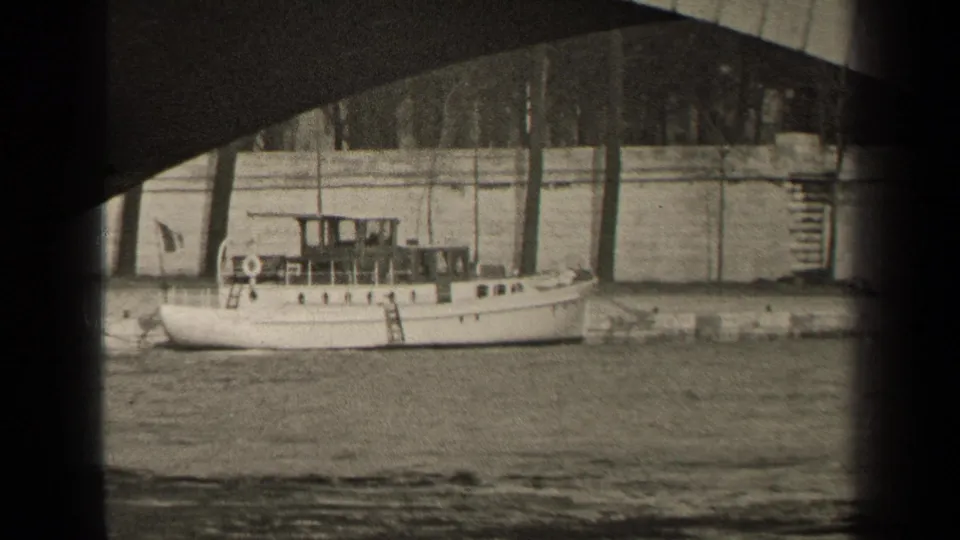 1947 Paris frame with a white riverboat beside the Seine embankment, partly framed by the dark underside of a bridge.