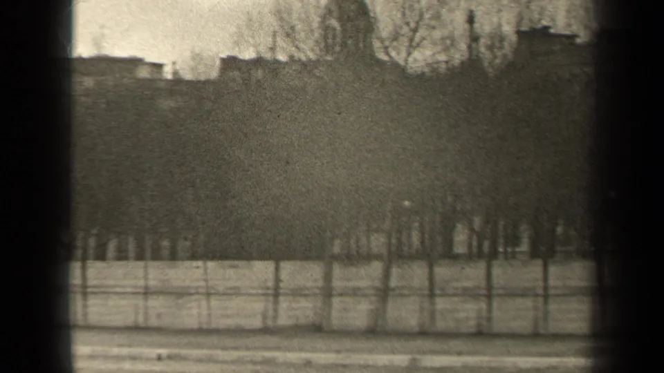 1947 Paris home-movie frame showing bare tree rows, a low fence, and the upper edge of a stone bridge on an overcast day.