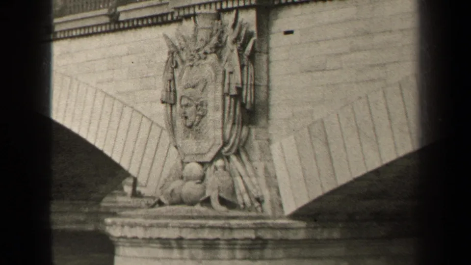 1947 Paris home-movie view of a sculpted bridge emblem, masonry arch, parapet, and dark film gate edges.