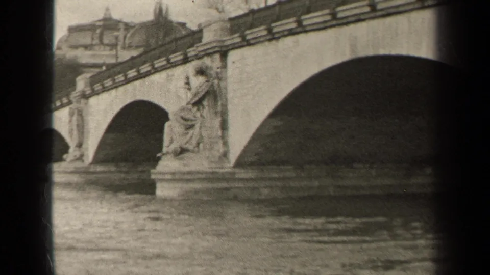 1947 Paris 8mm frame showing multiple bridge arches, sculptural figures, river surface, and buildings beyond the bridge.